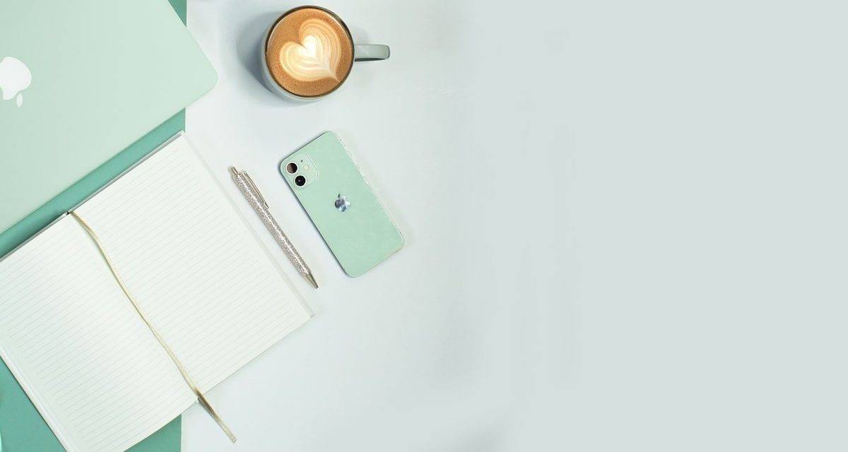 ミントグリーンのスマホとノート、ラテが並ぶ机