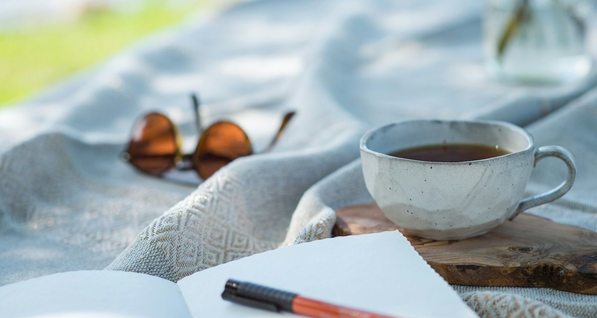 明るい布の上の、紅茶のカップと白いノートと赤いペン