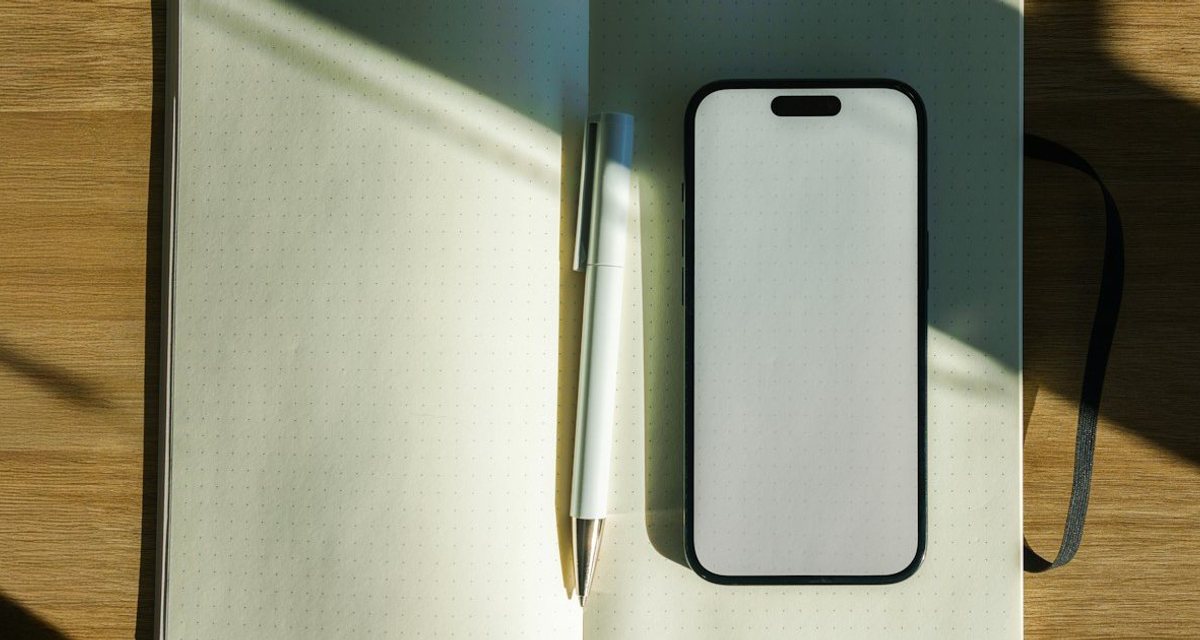 日差しの当たる木の机の上の開いたノートとスマホ